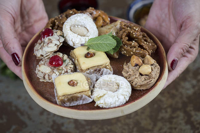 Mains féminines tenant des bonbons marocains typiques avec du miel et des amandes sur une assiette en bois — Photo de stock