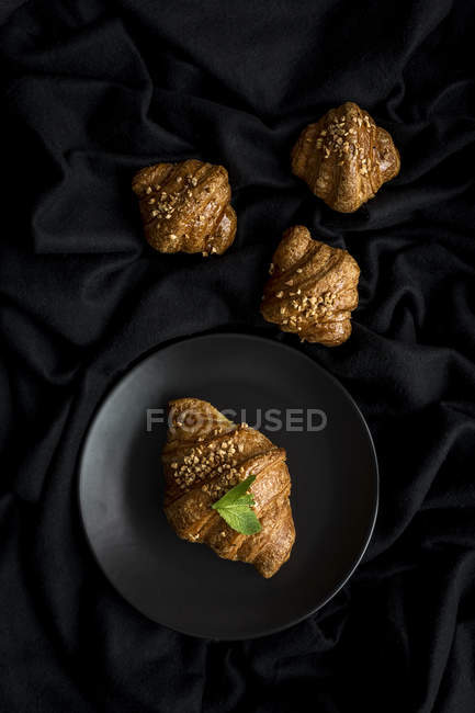 Croissant al forno su piatto e su tessuto nero — Foto stock