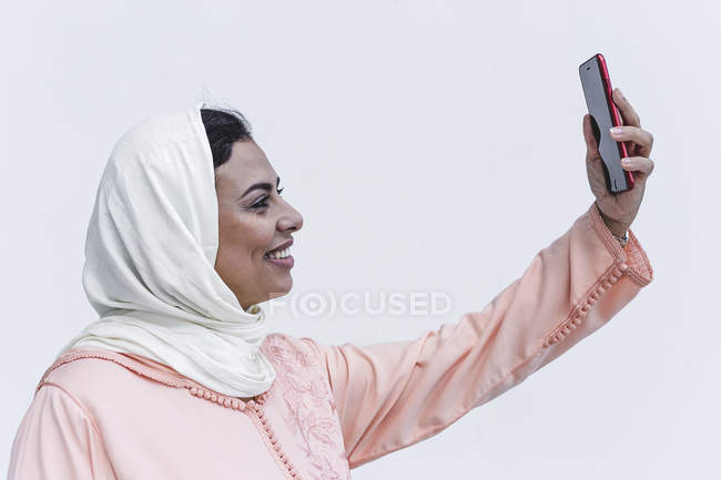 Sorridente donna marocchina con hijab e tipico abito arabo scattare selfie su sfondo bianco — Foto stock