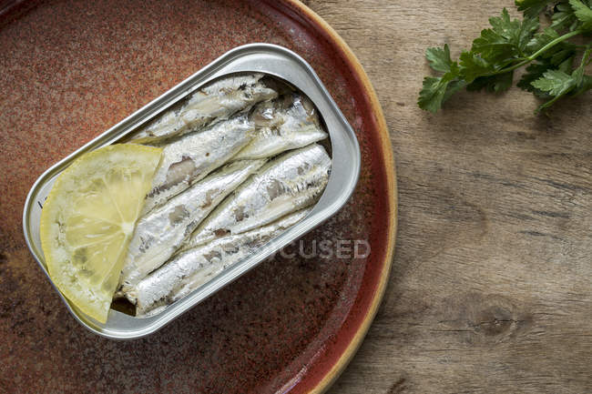 Canned sardines on brown plate with lemon — Stock Photo
