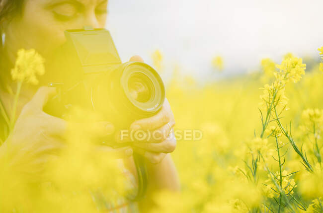 Mulher câmera retro fazendo foto na natureza com flores amarelas de perto — Fotografia de Stock