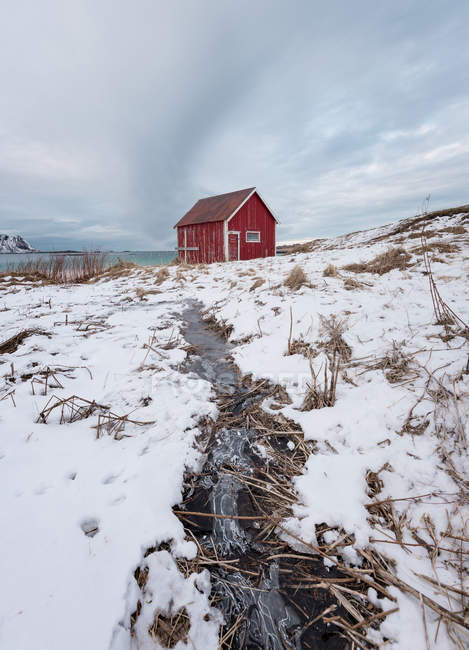 Rote Holzhütte am schneebedeckten Ufer im Winter — Stockfoto