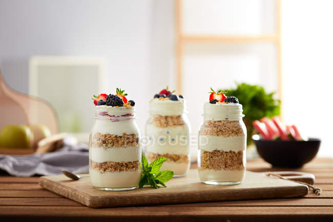Pots en verre avec granola et yaourt sur panneau en bois — Photo de stock