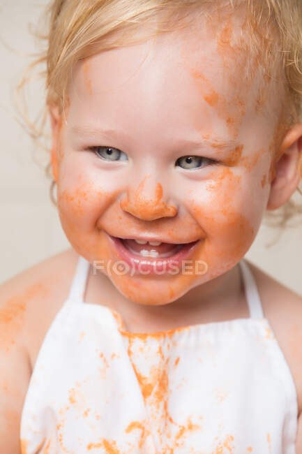 Fröhlicher Kleinkind-Junge in Schürze mit schmutzigem, mit Sauce überzogenem Gesicht. — Stockfoto
