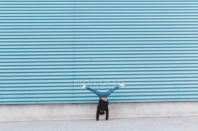 Неузнаваемый человек стоит на руках у голубой металлической стены — стоковое фото