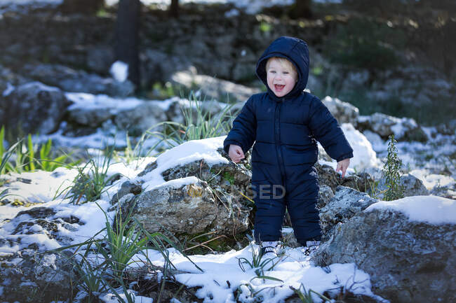 Cheerful little toddler boy looking at camera and holding snowball in nature. — Stock Photo