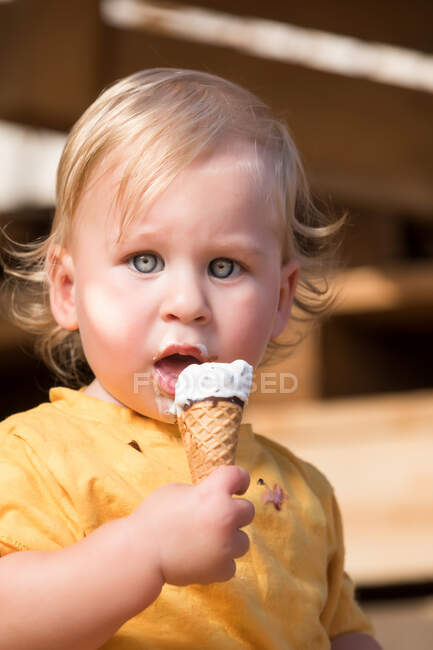 Молодий хлопчик в жовтому одязі їсть шоколадне морозиво з вафельним конусом . — стокове фото