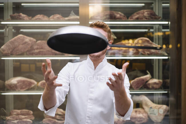 Chef cook in glasses and white gown throwing up frying pan working in restaurant. — Stock Photo
