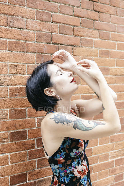 Чуттєва брюнетка жінка в візерунковому платті, що стоїть поруч з цегляною стіною — стокове фото
