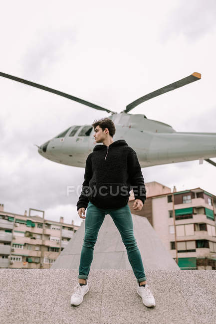 Bonito jovem em pé em frente ao monumento de helicóptero na rua da cidade — Fotografia de Stock