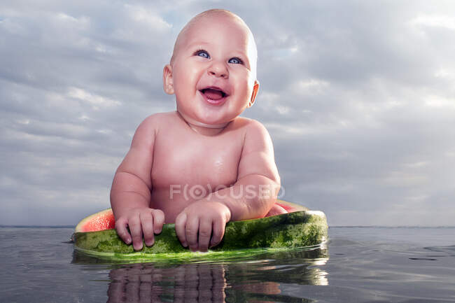 Веселый голый мальчик, сидящий в арбузе на воде — стоковое фото