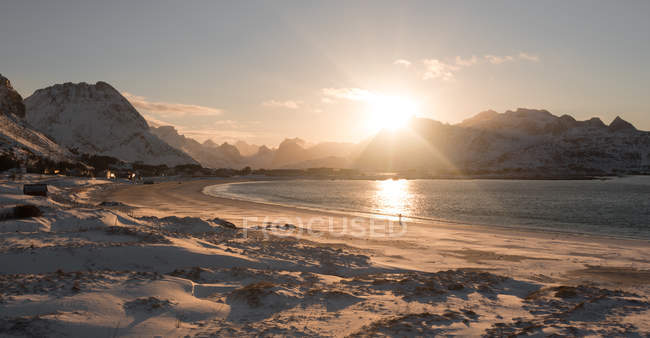 Снежная береговая линия с песчаным пляжем и морем в солнечном свете на фоне гор, Лофотен, Норвегия — стоковое фото