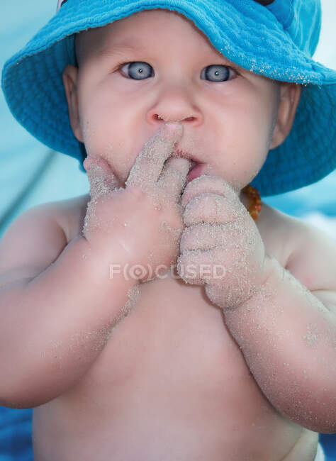 Young toddler boy in Panama hat licking fingers with sand and looking at camera. — Stock Photo