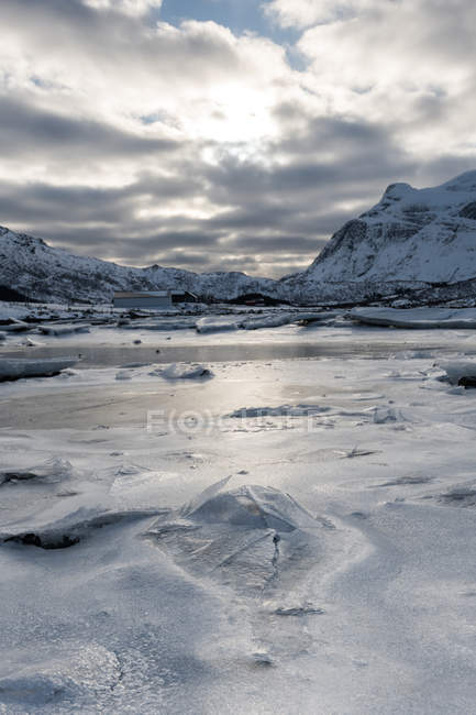 Cracked ice layer on water with snowy mountains — Stock Photo