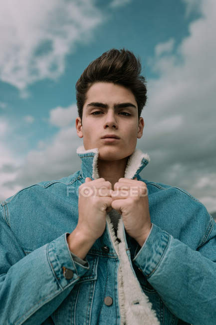Retrato de jovem adolescente na jaqueta de ganga elegante em pé no fundo do céu nublado — Fotografia de Stock