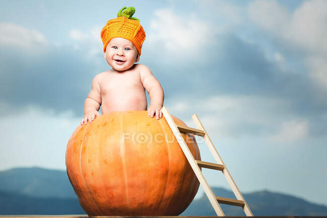 Очаровательный малыш, стоящий в большой тыкве с лестницей.. — стоковое фото