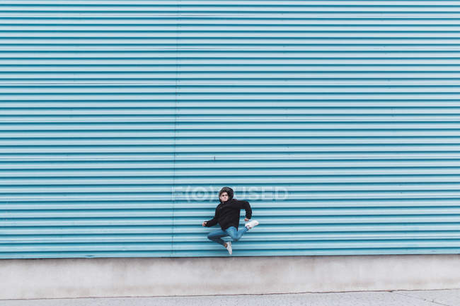 Hombre saltando contra la pared de metal azul en la calle de la ciudad - foto de stock