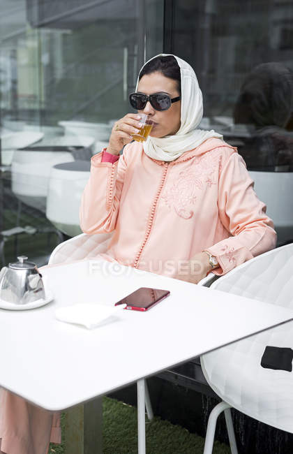 Марокканская женщина с хиджабом и типичным арабским платьем пьет чай в кафе — стоковое фото