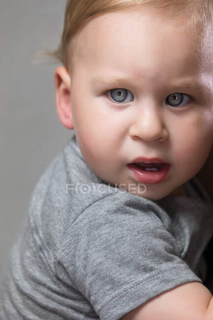 Portrait of adorable little toddler looking at camera on gray background. — Stock Photo
