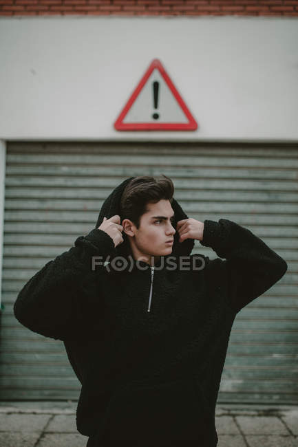 Teenager standing on street with exclamation sign and putting on hood — Stock Photo