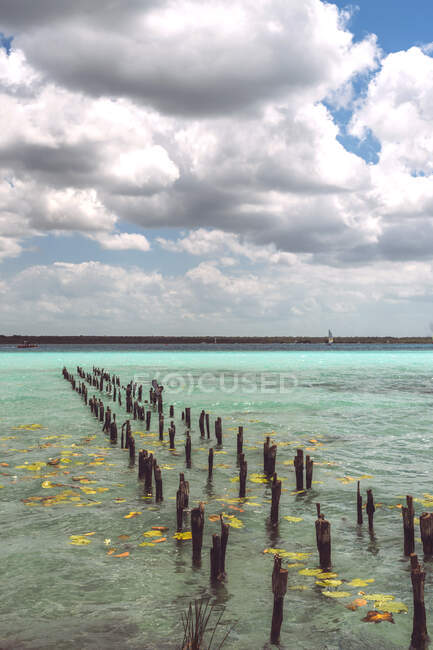 Rows of rotting stakes standing in turquoise Caribbean sea in cloudy day — Stock Photo