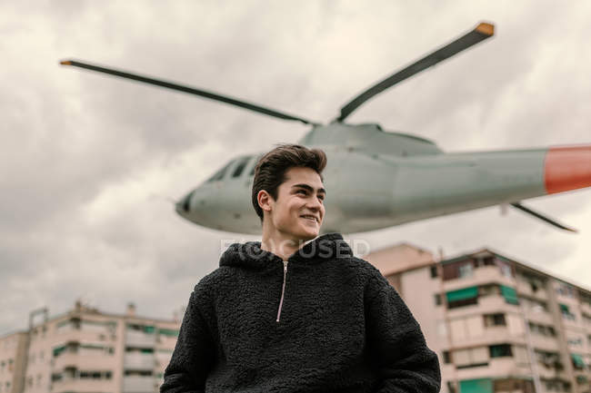 Ridendo giovane uomo in piedi al monumento elicottero sulla strada della città — Foto stock