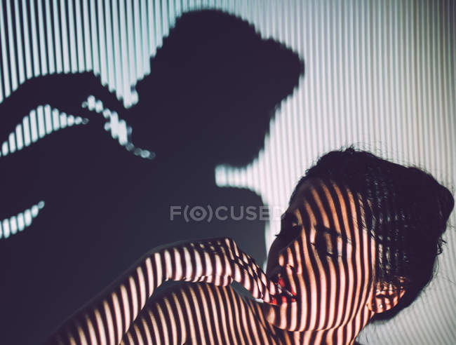 Seductive young woman with red lips and striped shadow on face and body posing in studio — Stock Photo