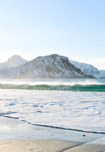 Cracked ice layer on water with mountains under blue sky — Stock Photo