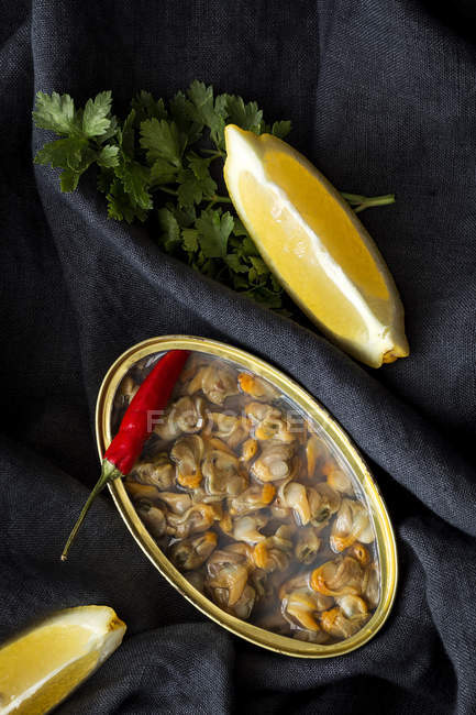 Boite de conserve aux délicieux fruits de mer servie avec piment et citron sur tissu noir — Photo de stock