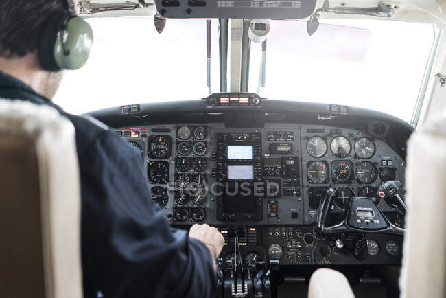 Неузнаваемый человек в наушниках пилотирует самолет? в одиночку, сидя в кабине современного самолета — стоковое фото