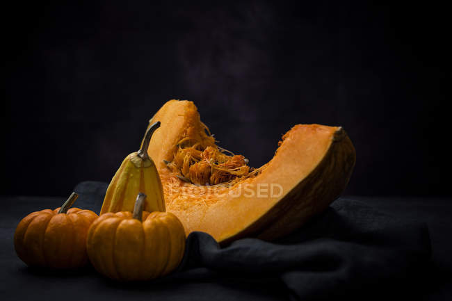Fresh whole pumpkins with piece on cloth on black background — Stock Photo