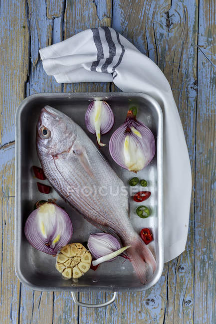 Сырой морской лещ в сковороде с овощами на деревянном столе — стоковое фото