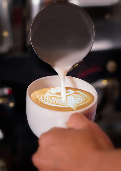 Crop hand of unrecognizable bartender pouring cream to latte and drawing a flower. — Stock Photo