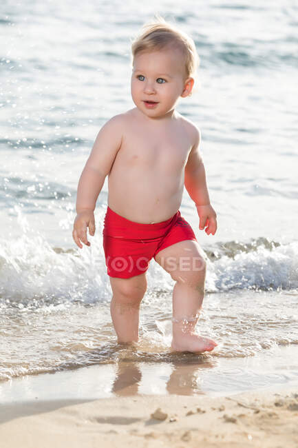 Menino adorável andando na praia de areia e olhando para a beira-mar. — Fotografia de Stock