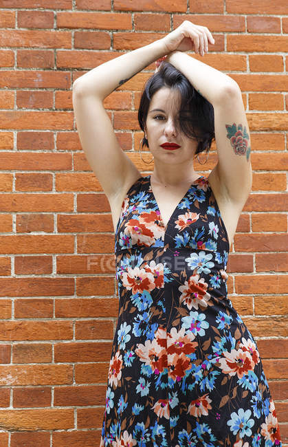 Tätowierte Frau in gemustertem Kleid steht vor Backsteinmauer — Stockfoto