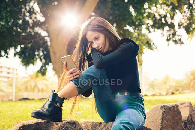 Молода жінка сидить на скелі і використовує смартфон у парку — стокове фото