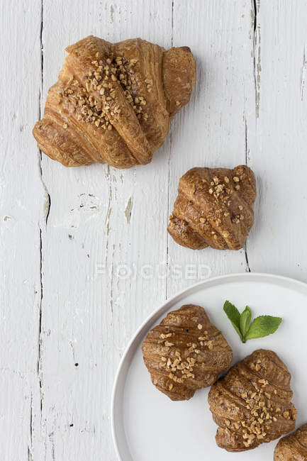 Croissants cozidos no prato e na mesa de madeira branca — Fotografia de Stock