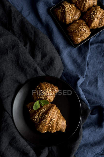 Gebackene Croissants in Schale und auf Teller auf schwarzem Stoff — Stockfoto