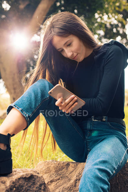 Junge Frau sitzt auf Felsen und benutzt Smartphone im Park — Stockfoto