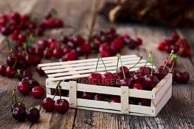 Primer plano de la caja de madera de deliciosas cerezas maduras en madera marrón - foto de stock