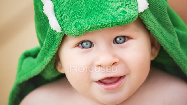 Adorable toddler boy looking at camera and sitting in green colored towel. — Stock Photo