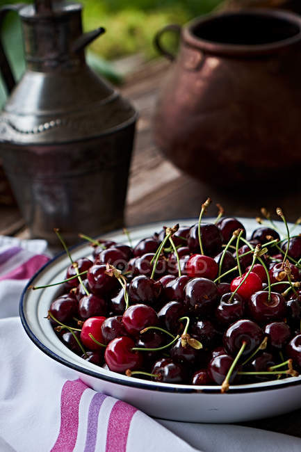 Close-up of fresh cherries in metal bowl on brown wooden table — Stock Photo