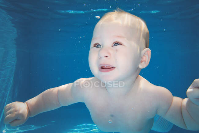 Underwater shot of little boy diving in deep blue pool in sunny day. — Stock Photo