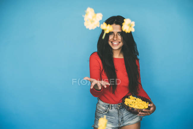 Junge Frau steht und wirft Blumen auf blauem Hintergrund — Stockfoto