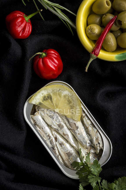Canned fish and hot peepers with bowl of olives on black cloth — Stock Photo