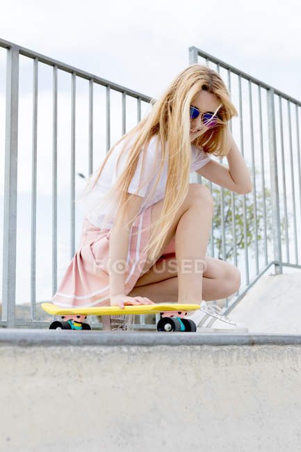 Fille blonde élégante et souriante en lunettes de soleil avec penny board dans le skate park — Photo de stock