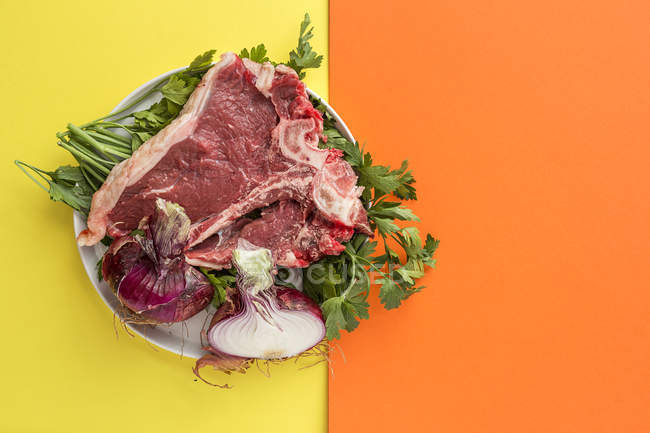 Raw beef steak with ingredients on plate on yellow and orange background — Stock Photo