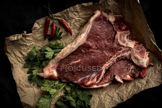 Raw beef steak on parchment with ingredients on black background — Stock Photo