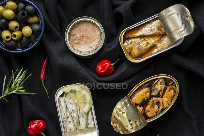 Bowl with olives and various canned fish and seafood on black cloth — Stock Photo