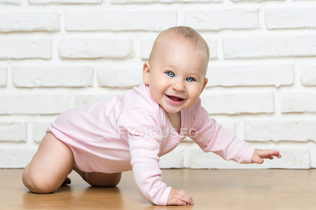 Cheerful little toddler looking at camera and crawling on background of white brick wall. — Stock Photo